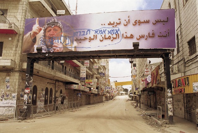 Plakat s palestinskim voditeljem Jaserjem Arafatom, kljub izraelskim vojakom, še vedno visi v središču prazne Ramale. Plakat s palestinskim voditeljem Jaserjem Arafatom, kljub izraelskim vojakom, še vedno visi v središču prazne Ramale.