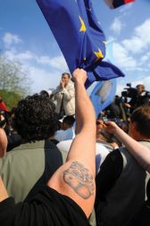 Tetovaža lobanje z nacistično čelado na shodu na mostu čez Dragonjo aprila 2008. V ozadju protestnike nagovarja Marjan Podobnik.
