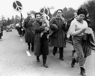 Znak za mir na enem svojih prvih protestnih pohodov v aprilu 1958. Na poti od Londona do Aldermastona so ga uporabili člani britanskega gibanja, ki se je zavzemalo za jedrsko razorožitev. Gibanje je tudi naročilo izdelavo znaka, ki ga je Gerald Holtom oblikoval tako, da je v njem ujel črki N in D, v takšni obliki, kot predvideva abeceda iz signalov, narejenih z zastavami. Zakaj je izbral črki N in D? Ker je angleški izraz za jedrsko razorožitev &raquo;nuclear disarmament&laquo;. Priponko s tem simbolom je ob svojem obisku Anglije leta 1960 odkril dr. Philip Altbach, ki je bil tedaj še študent. Odnesel jo je v ZDA in na njegovo pobudo je znak začelo uporabljati ameriško študentsko gibanje. Danes je znak mednarodni simbol miru.