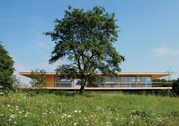 Lesena hiška na Gradiščanskem v Avstriji (Artec Architekten, 2006) Drevo in hiša, vertikala in horizont, natura in kultura, nebo in zemlja: arhetipski dialogi med komplementarnimi dvojicami bivanja, kreacije in kompozicije. Minimalna longitudinalna hiška, ki skoraj lebdi na robu panonske pokrajine, stoji na samem, zunaj ožje določujočega konteksta, zato je moderna, abstraktna in odprta proti jugu ter zaprta proti severu. Z velikimi napušči, ki ustvarjajo široko bivalno teraso med znotraj in zunaj, z zaščito pred soncem in dežjem. Lesena hiška na Gradiščanskem v Avstriji (Artec Architekten, 2006) Drevo in hiša, vertikala in horizont, natura in kultura, nebo in zemlja: arhetipski dialogi med komplementarnimi dvojicami bivanja, kreacije in kompozicije. Minimalna longitudinalna hiška, ki skoraj lebdi na robu panonske pokrajine, stoji na samem, zunaj ožje določujočega konteksta, zato je moderna, abstraktna in odprta proti jugu ter zaprta proti severu. Z velikimi napušči, ki ustvarjajo široko bivalno teraso med znotraj in zunaj, z zaščito pred soncem in dežjem.